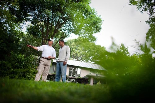 The gentlemen speaking with tree and house in the backround